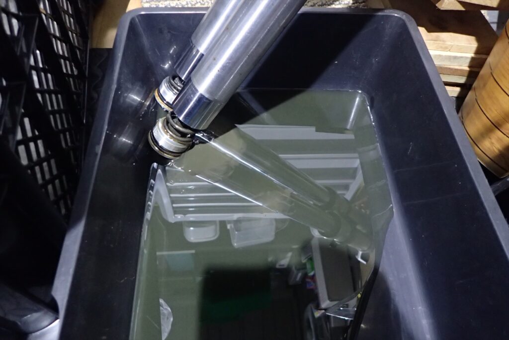 Draining dirty old fork oil from inverted front forks into a plastic oil pan.