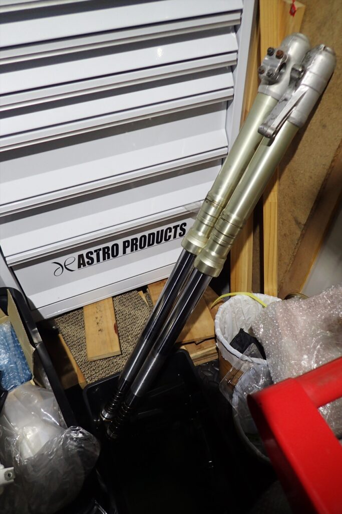 A pair of Honda XR250R ME08 conventional front forks set in a garage workshop for a fluid change.