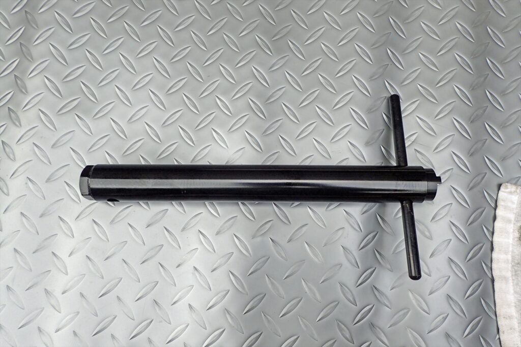 A specialized front fork cylinder cartridge holder tool with a T-handle used for motorcycle suspension overhaul.