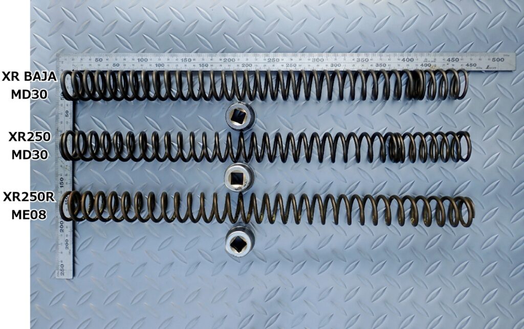 Comparison of front fork springs from Honda XR250 MD30, XR BAJA MD30, and XR250R ME08 aligned with a metal ruler and socket tools for stability.