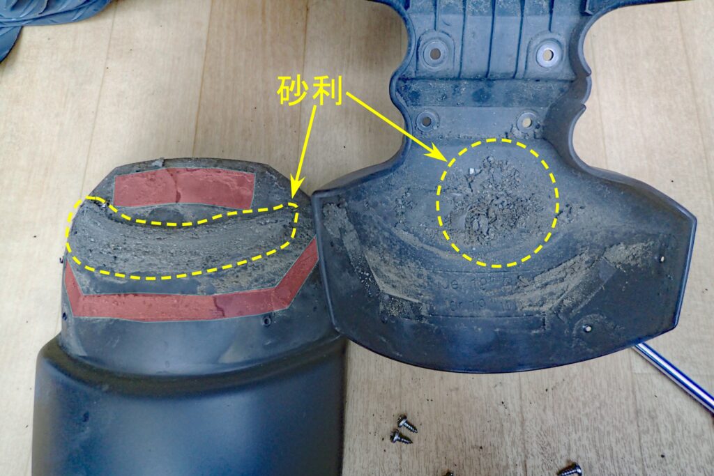Close-up of accumulated sand and gravel trapped in the gap of a motorcycle fender extender, annotated to explain the increase in unsprung weight.