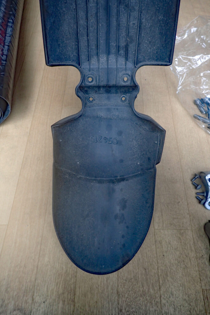 Inner underside view of the BMW G650GS front fender, showing four screws and double-sided tape used to fix the extension flap.
