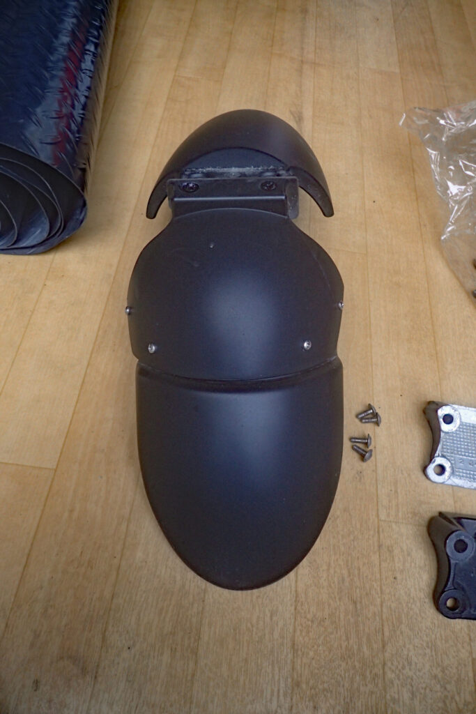 The original black front fender of a BMW G650GS motorcycle removed from the vehicle and laid flat on the floor with mounting screws removed.