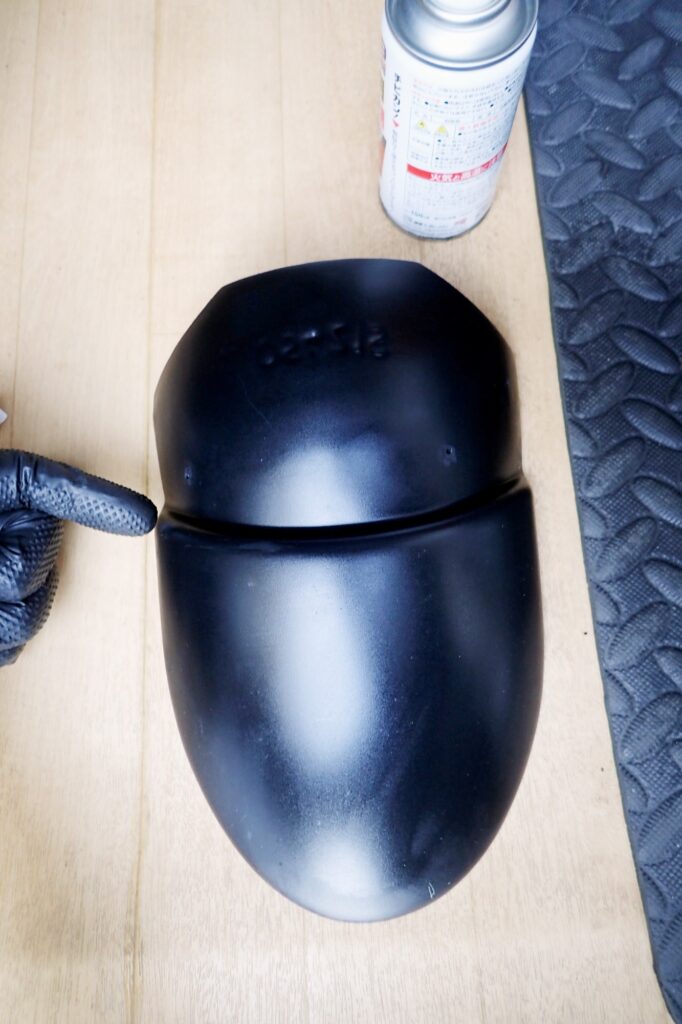 A person wearing black nitrile gloves wiping the plastic fender extender surface clean using a white Kimwipe.