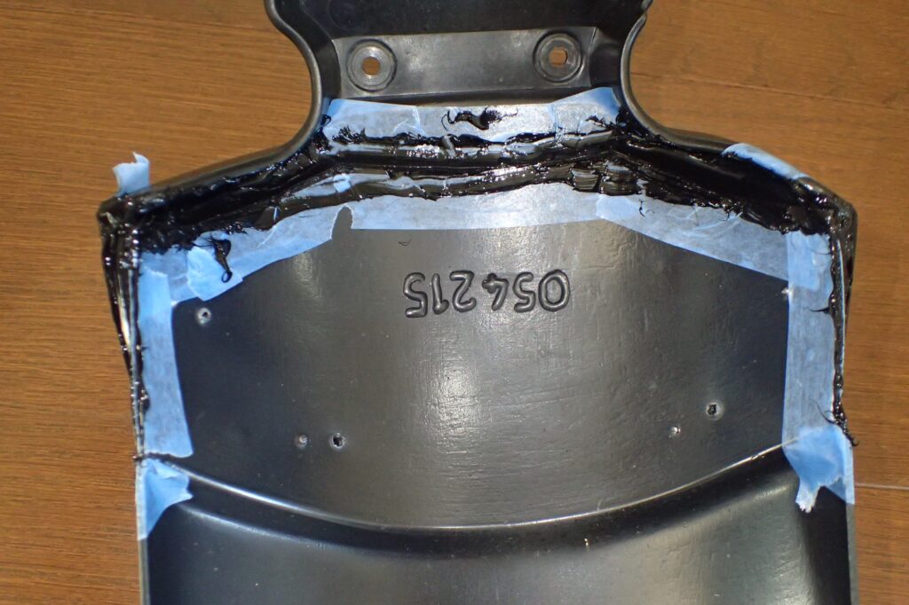Black silicone waterproof caulk injected straight into the joint gap on the inner side of a motorcycle fender.