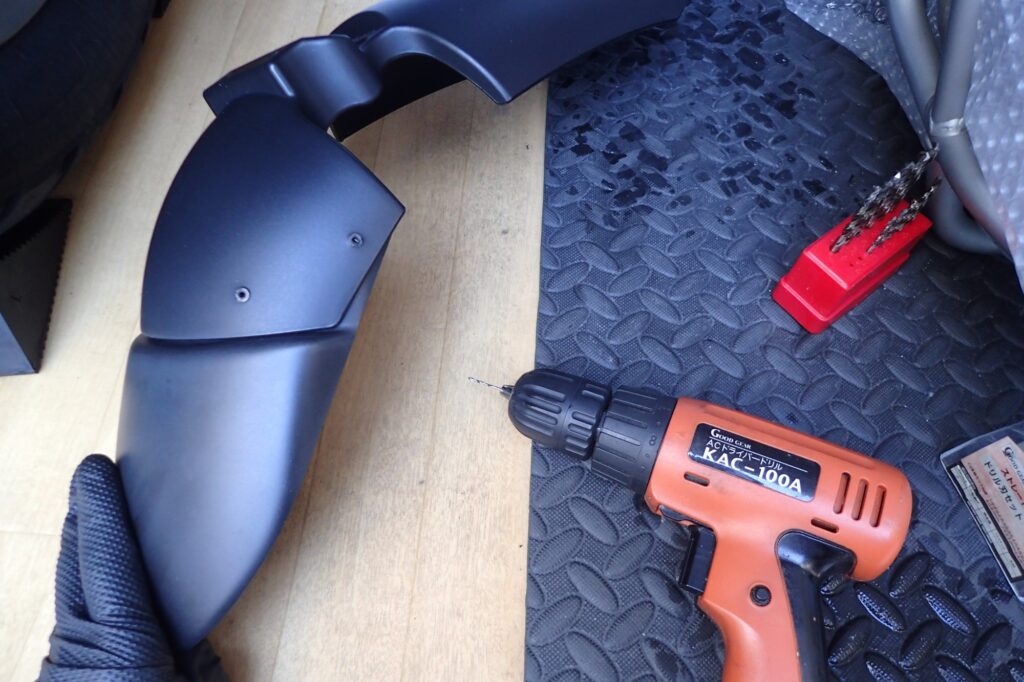 A person using an orange electric drill driver to carefully make screw holes on a black BMW G650GS front fender.