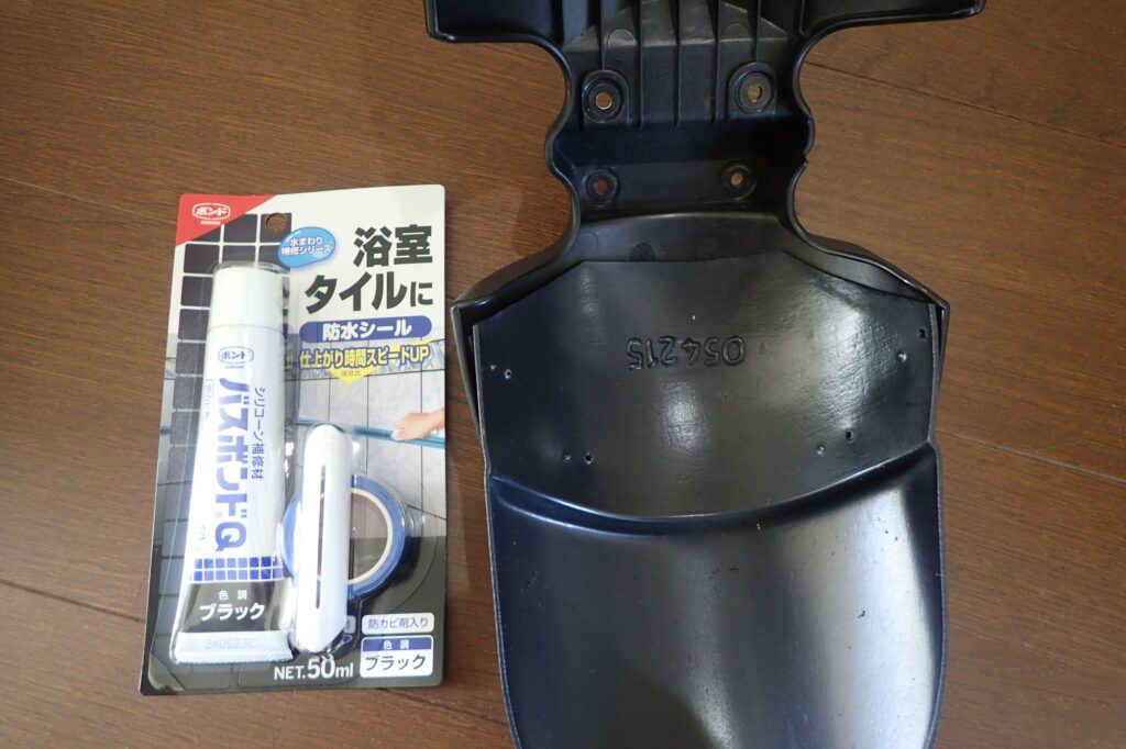 A package of Konishi Bathbond Q black waterproof silicone sealant placed next to the underside of a motorcycle fender.