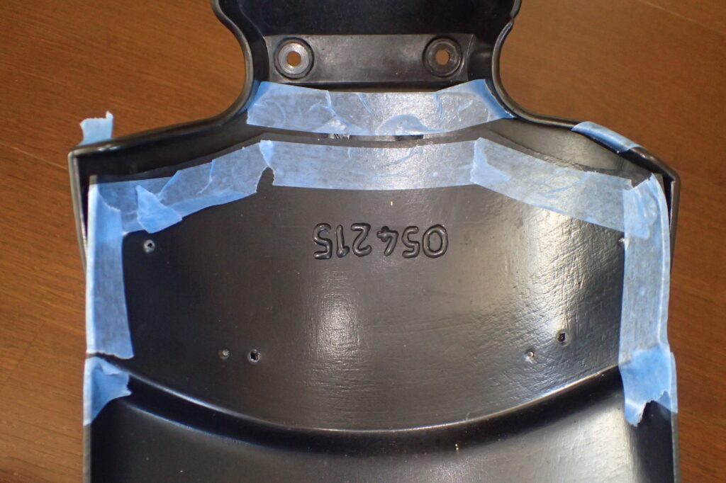 The inner underside of a motorcycle fender carefully masked with blue tape along the edges where the extender overlaps.