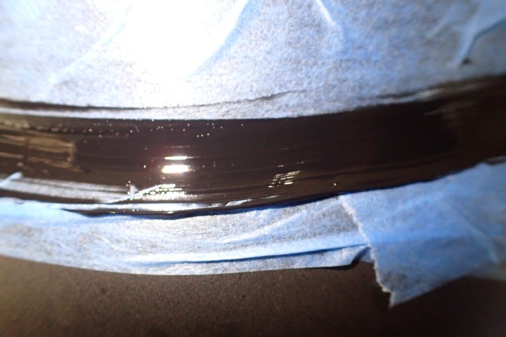 Smoothing out the injected black silicone sealant inside the motorcycle fender joint using a finger to ensure a perfect seal.