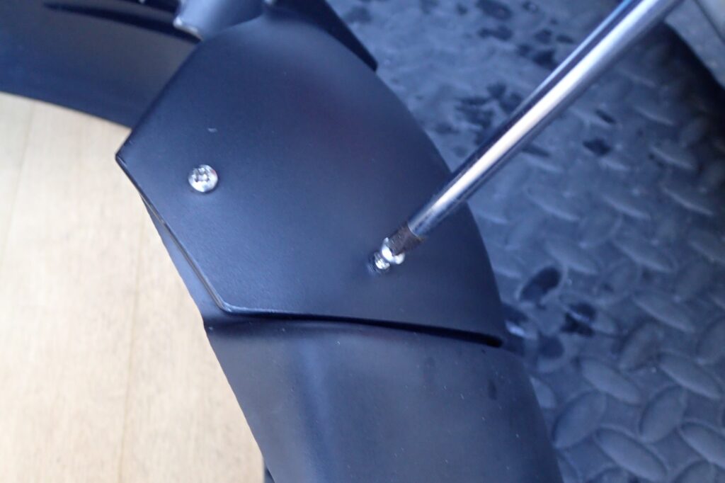 Tightening a stainless steel screw into the front fender extender using a plus screwdriver for secure mechanical attachment.