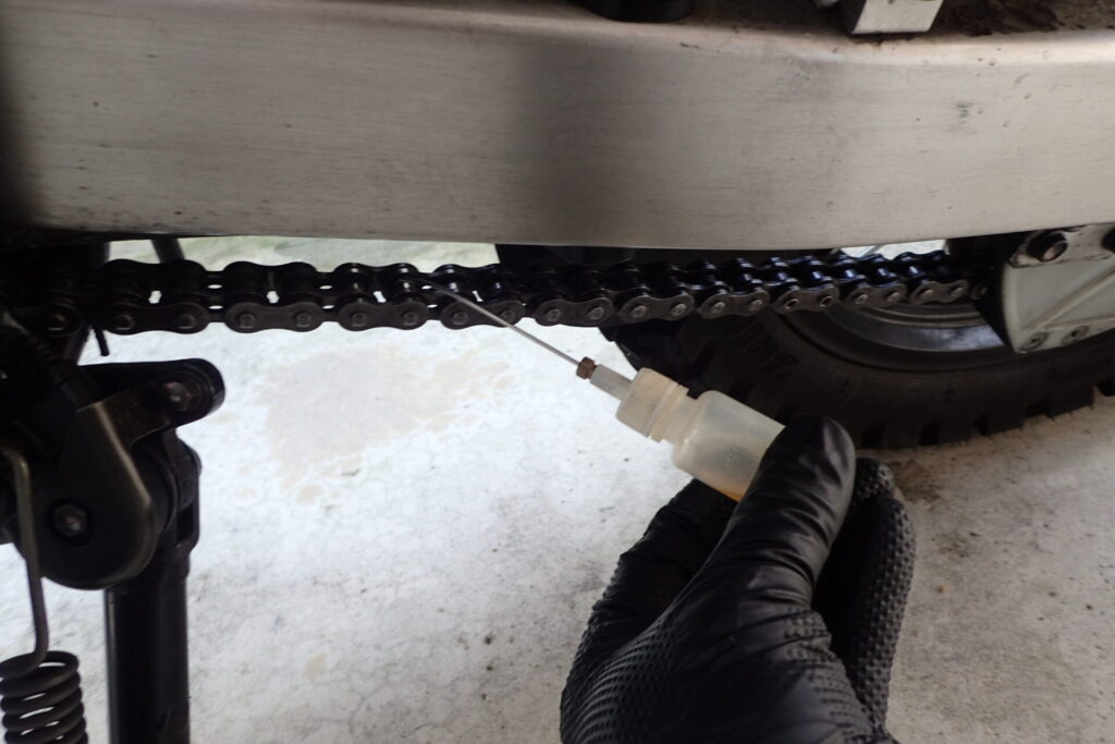 AZの狭所用オイラーで,バイクのチェーンに給油する様子