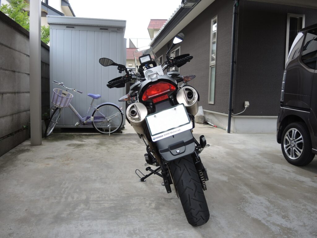 ガレージまたは駐車スペースに停められたBMW G650GSの後方からの全景写真です。バイクには、社外品の延長フェンダーが装着されており、すっきりとしたリアビューになっています。特徴的な二本出しのマフラーが写っています．