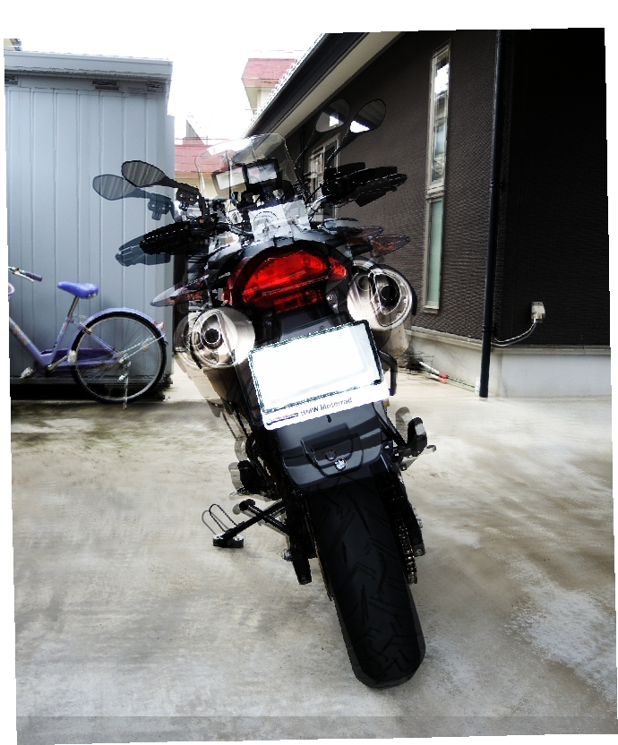 ガレージまたは駐車スペースに停められたBMW G650GSの後方からの全景写真です。サイドスタンドプレート取り付け前と後の写真を重ねて，取り付け前後の比較ができる写真です．