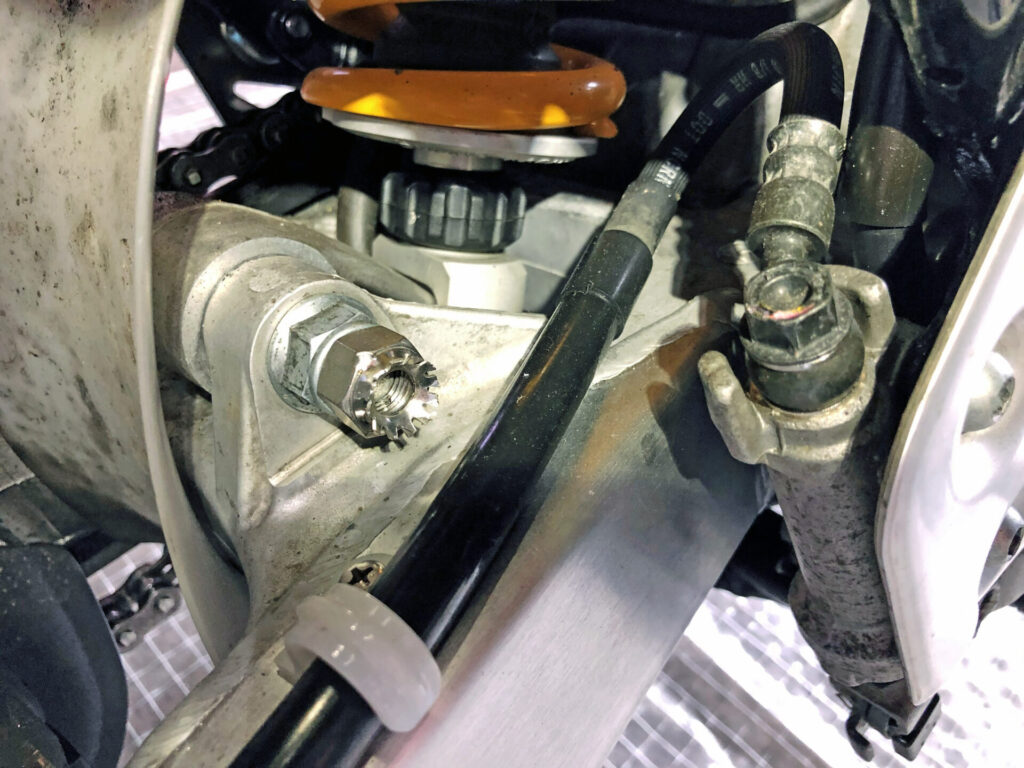 NGCスムーズドライブ(静電気除去システム)の除電ナットと割りピンが取り付けられた,バイクのスイングアームピボット部の詳細写真です。このチューニングにより、スイングアームの動きがスムーズになり、サスペンションの作動性や乗り心地の向上が期待されます。