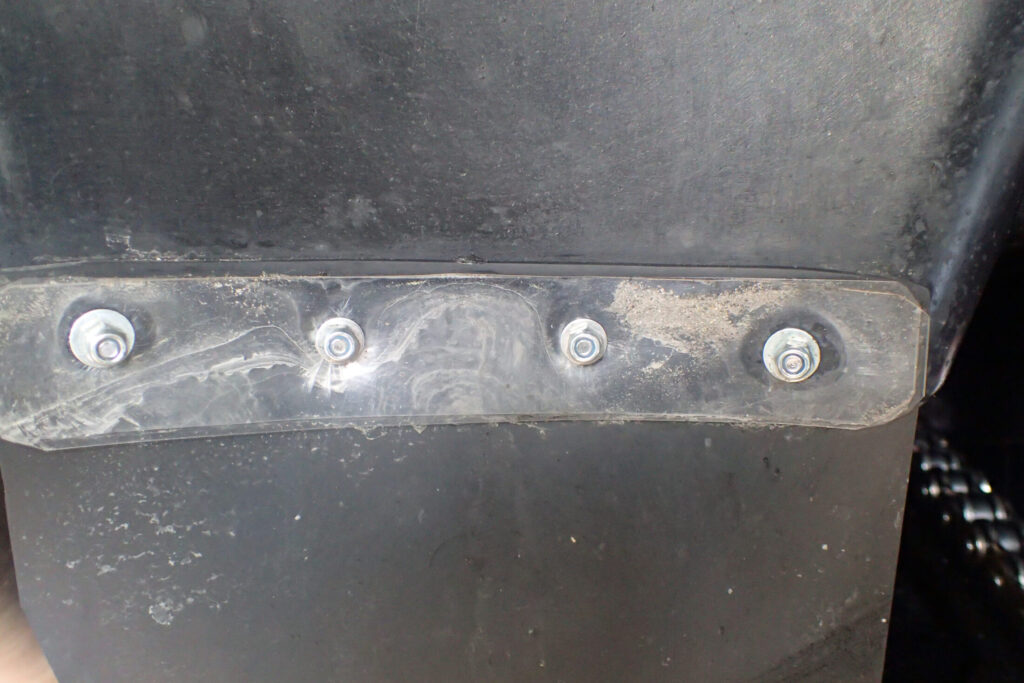 バイクのリアインナーフェンダーに取り付けられたマッドガード延長部の固定ディテール。ボルトと透明な補強プレートを使った取り付け方法のクローズアップ写真。