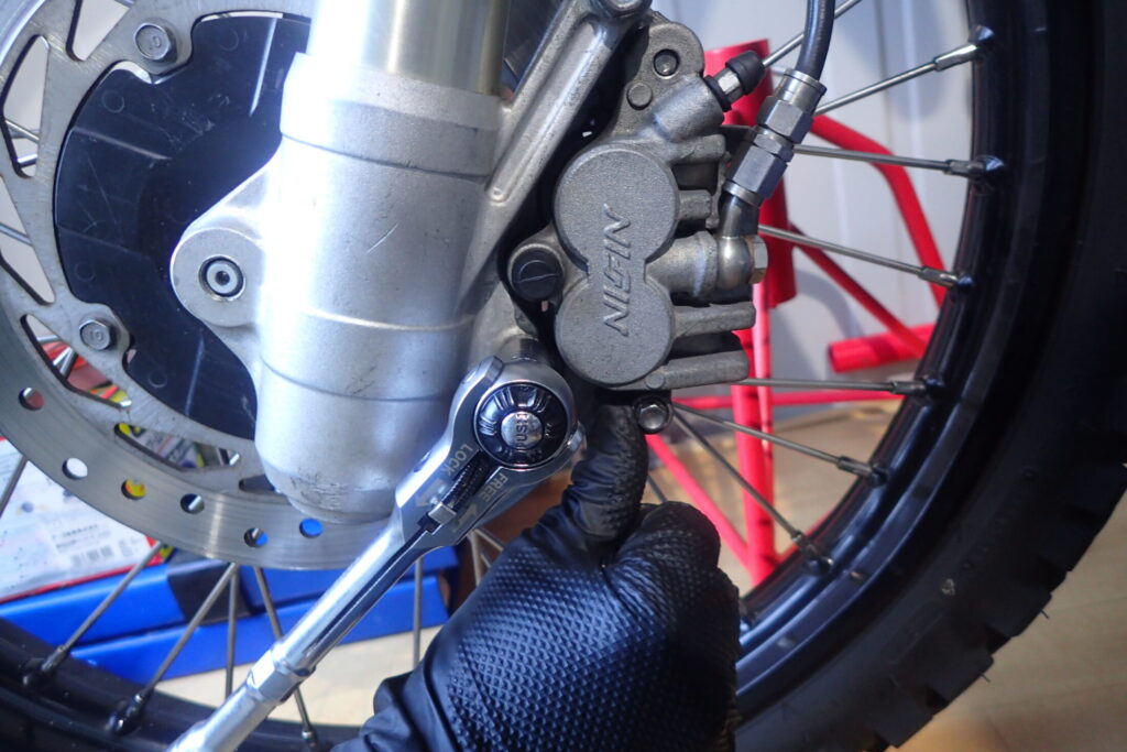 【トルク管理】 ブレーキキャリパーを車体に取り付け、規定トルクでボルトを締め付ける作業。ディスク回転方向に力を加えて固定する。