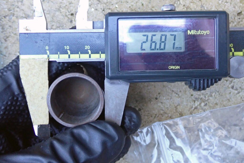 カシマコート（硬質潤滑アルマイト）を施したアルミ製ピストンの外径を精密測定（26.87mm）している様子。