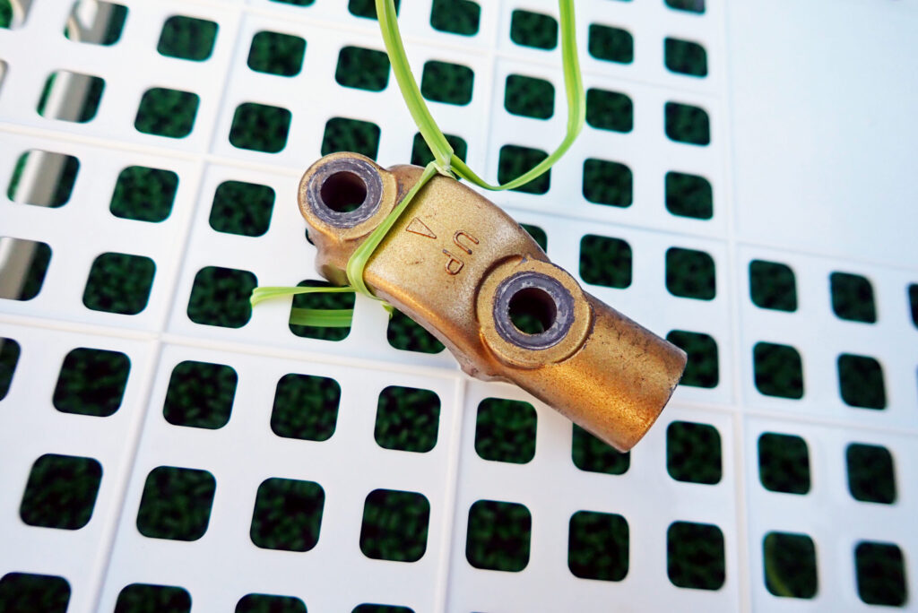 重曹ブラスト施工前の金色アルマイト加工されたアルミパーツ。表面には経年による油汚れや堆積物が付着している状態。