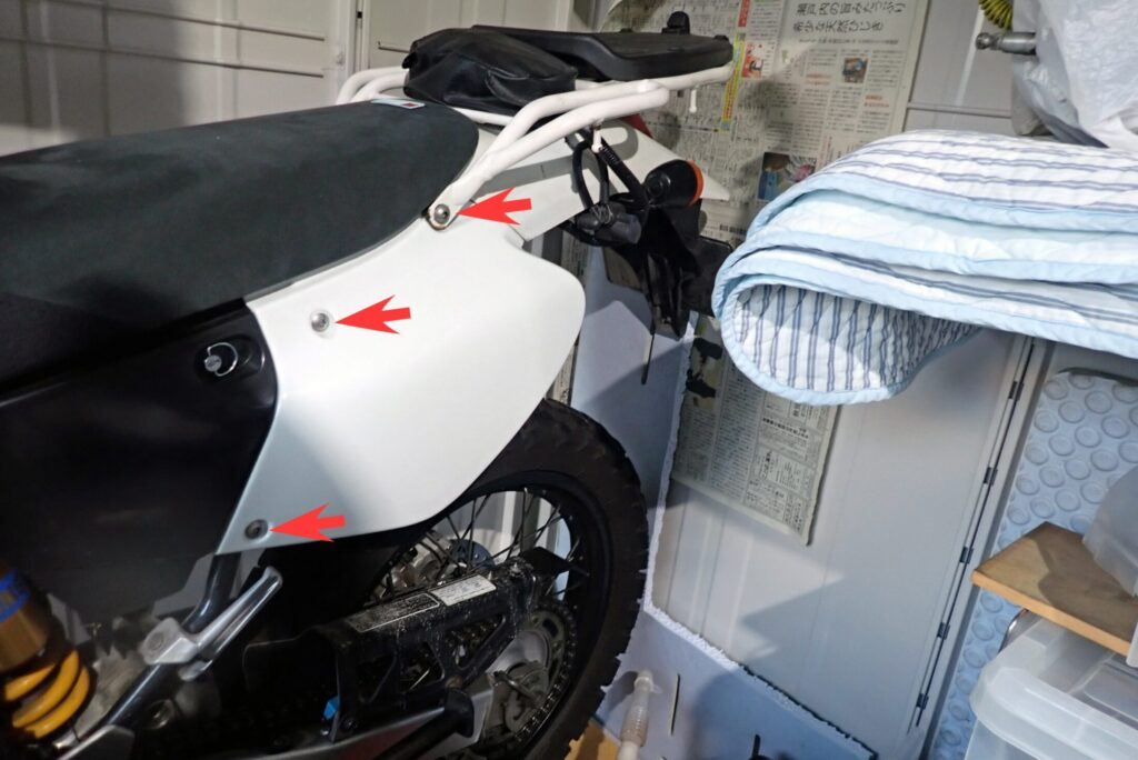 ホンダXR250 BAJAのバッテリーメンテナンスのため、左側のサイドカバーを固定しているボルトを取り外す様子
