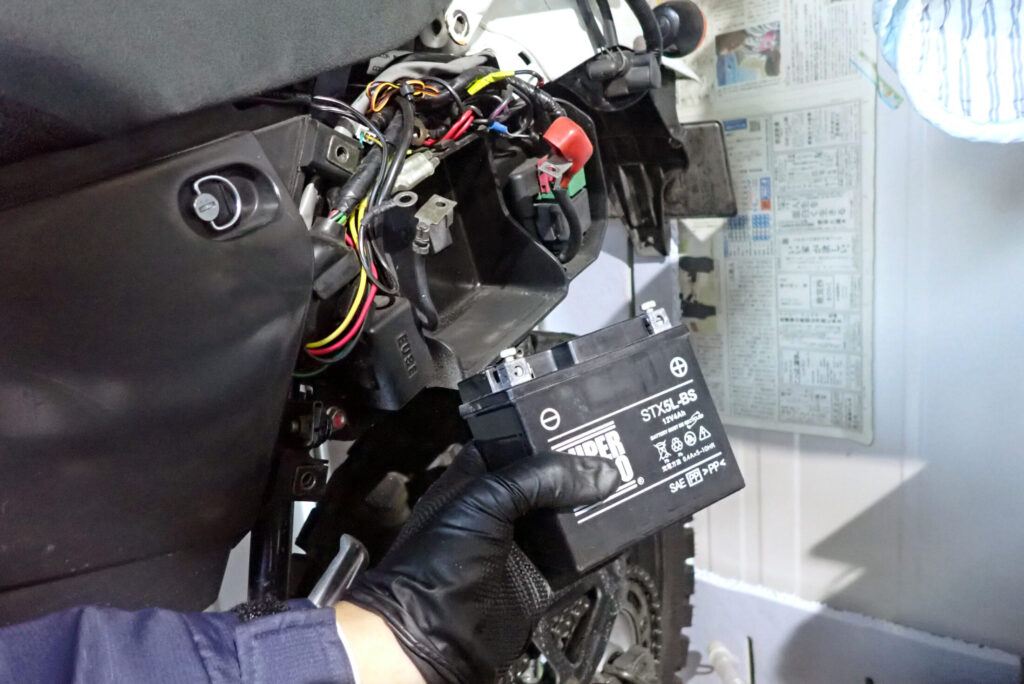 ハーネスの干渉に注意しながら、XR250 BAJAの狭いケース内からバッテリー本体をゆっくりと手前に引き出す作業