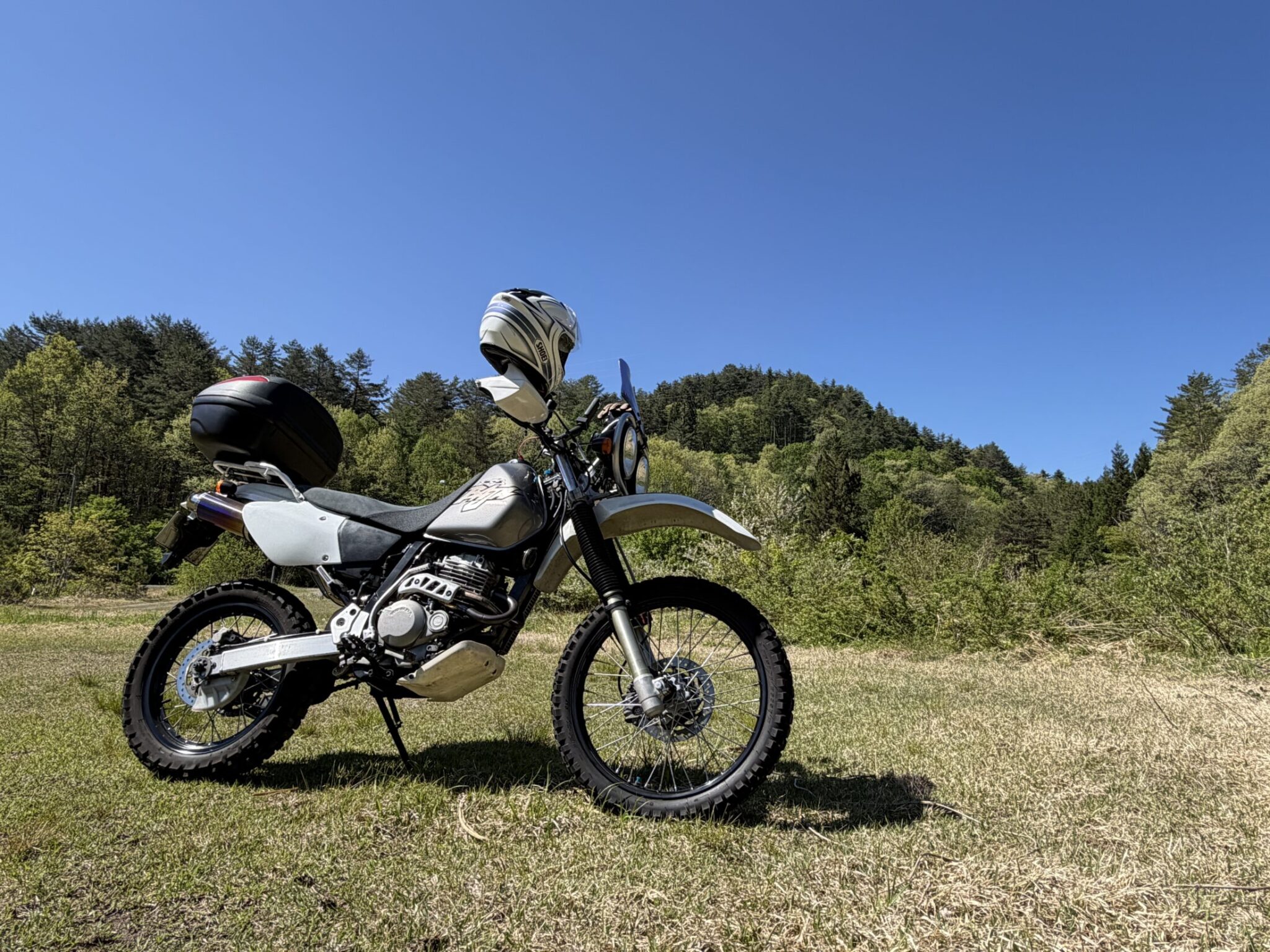 Honda XR250 BAJA parked on a grassy field with green mountains and blue sky