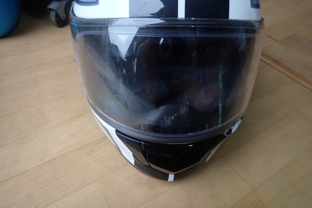 SurLuster Zero Finish liquid applied onto the visor surface of a SHOEI full-face helmet for cleaning.