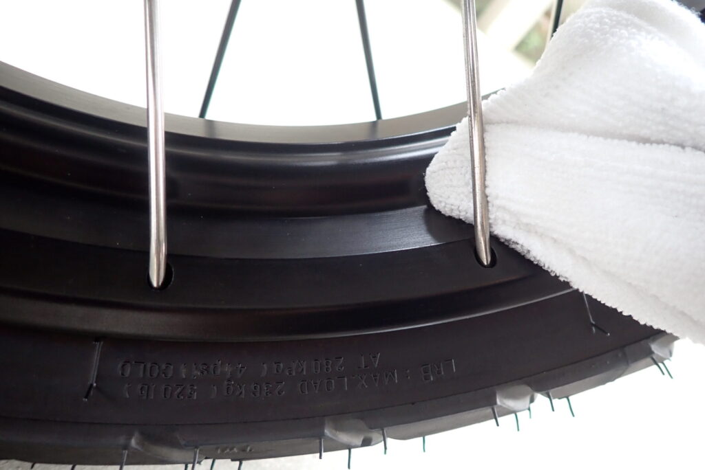 Cleaning the front wheel rim of a Honda X-ADV using a white microfiber cloth.