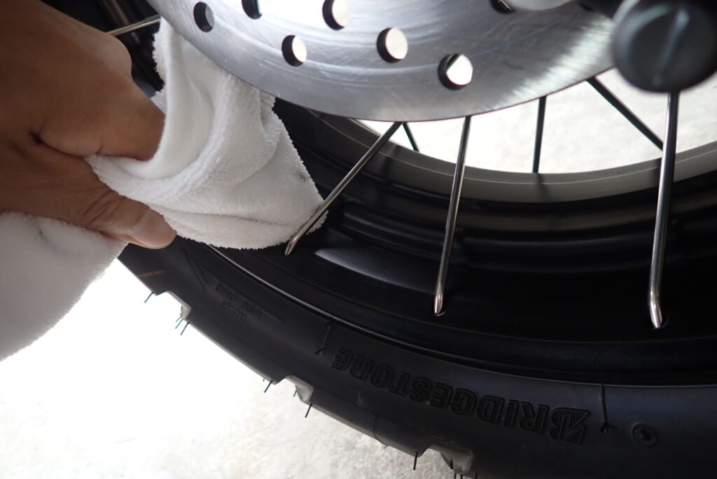 Wiping the tight space between the brake disc and the rim on a Honda X-ADV rear wheel with a microfiber cloth.
