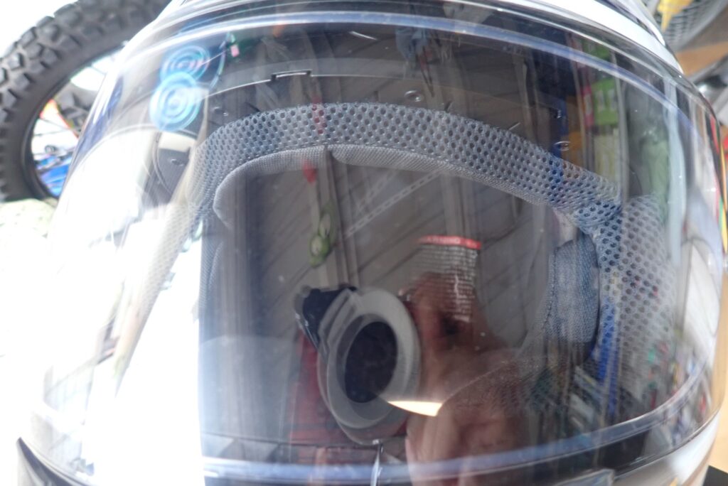 Close-up view of a dirty SHOEI motorcycle helmet visor with dust and smudge marks before cleaning.