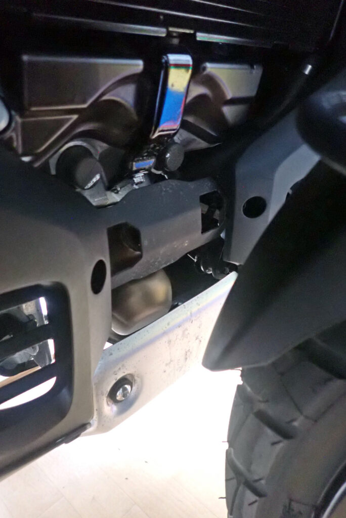 View of the front exhaust pipes and engine area behind the front tire of a Honda X-ADV 750, showing the area vulnerable to mud splashes.