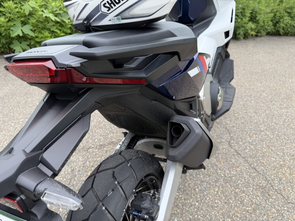 Rear right side view of a Honda X-ADV 750 after running on a wet surface, highlighting the exhaust muffler and rear indicator setup.