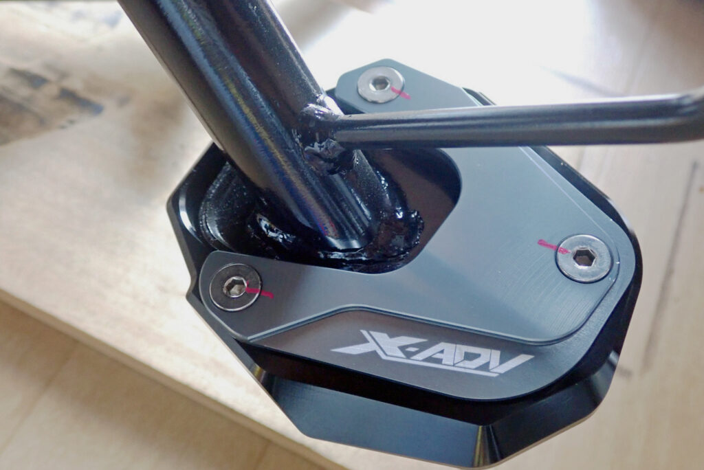 The side stand enlarger wide plate successfully installed on a Honda X-ADV 750 motorcycle, complete with pink alignment markings on the bolts.