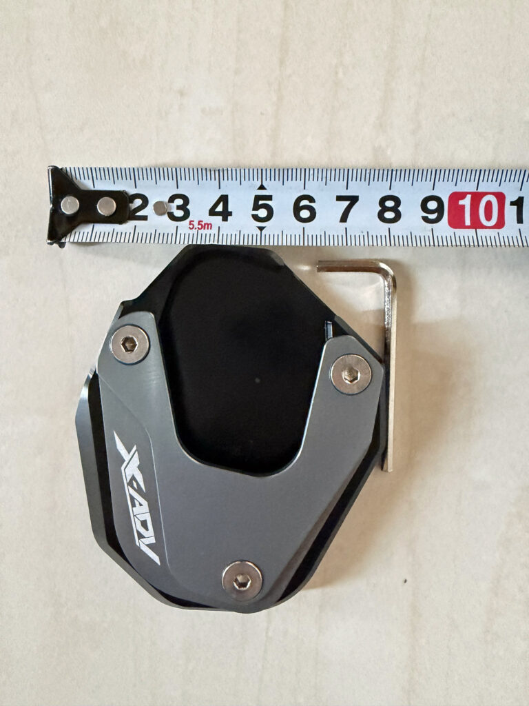 Top view of a Honda X-ADV 750 side stand enlarger pad, measuring the width with a tape measure.