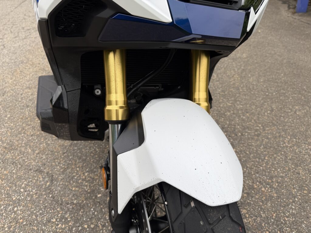 Front view of a Honda X-ADV showing fine dirt and mud water splashes on the white front fender and gold inverted forks.