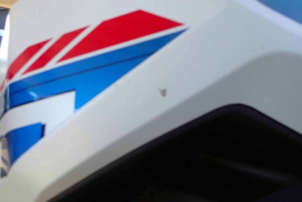 Close-up of a bug splat stain on the white front fairing of a Honda X-ADV motorcycle, showing dirt accumulated right after delivery.