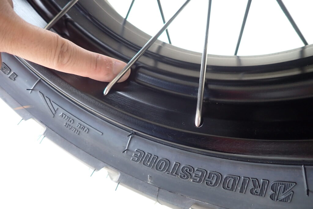 A finger pointing at the narrow spoke gap on the Honda X-ADV rear wheel, illustrating limited space for hands.