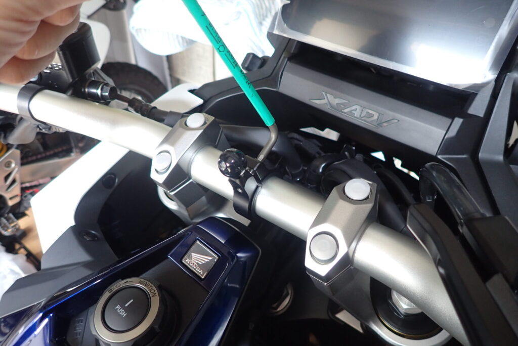 Tightening the aluminum ball mount onto the Honda X-ADV fatbar using a green Wera allen key tool.