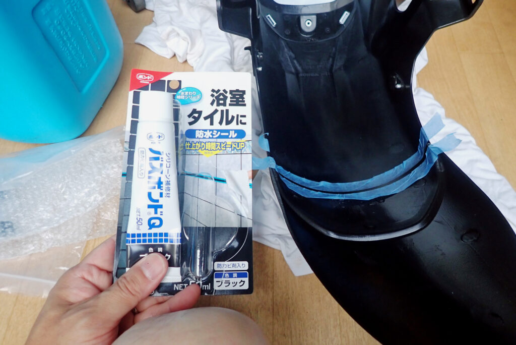 Holding a tube of Konishi black waterproof silicone sealant next to the masked inner joint of the motorcycle fender.