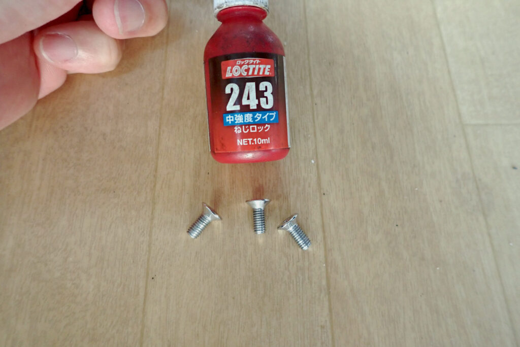 A bottle of Loctite 243 medium strength threadlocker liquid and three bolts for securing a motorcycle side stand plate.