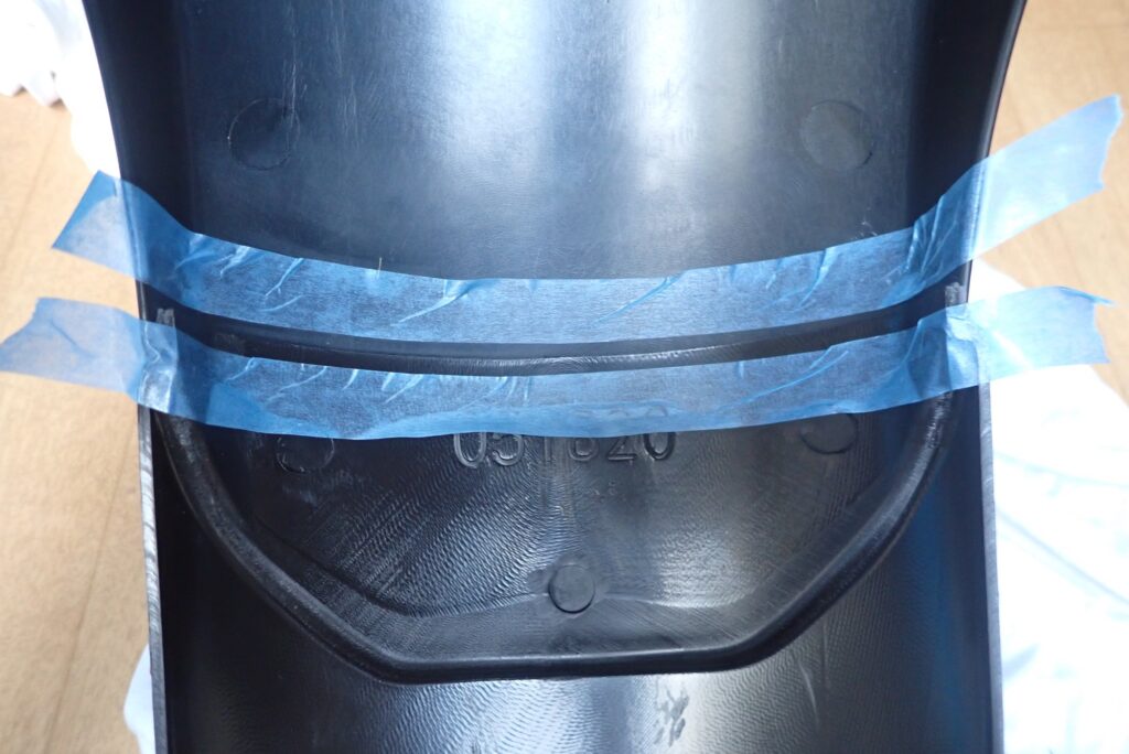 Blue masking tape applied along the joint line between the front fender and the extender on the inner side for caulking preparation.