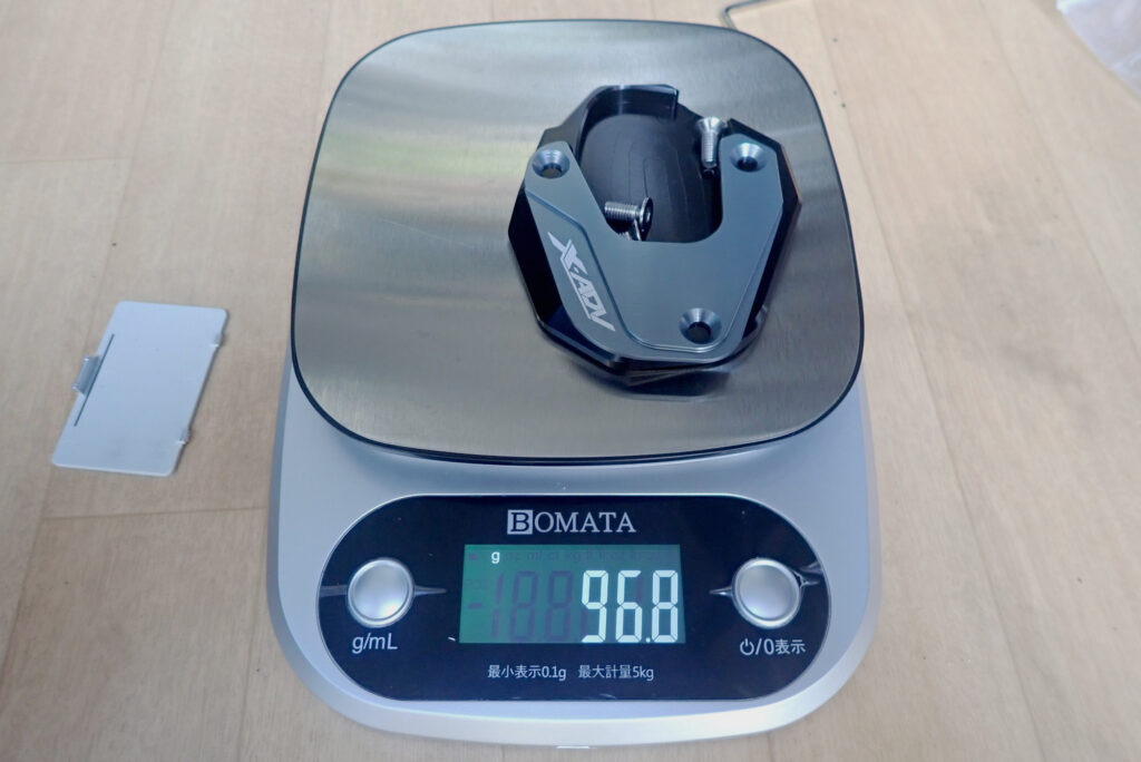Measuring the weight of a lightweight Honda X-ADV side stand enlarger plate on a digital kitchen scale showing ninety-six point eight grams.