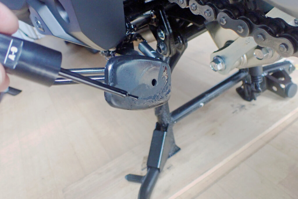 Applying black touch-up paint to the bottom of a Honda X-ADV side stand using a paint pen.