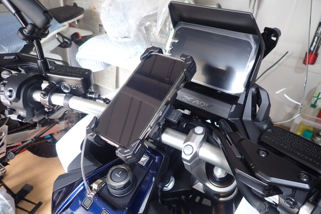 A smartphone securely mounted on the center of a Honda X-ADV handlebar, without obstructing the view of the 5-inch TFT display.