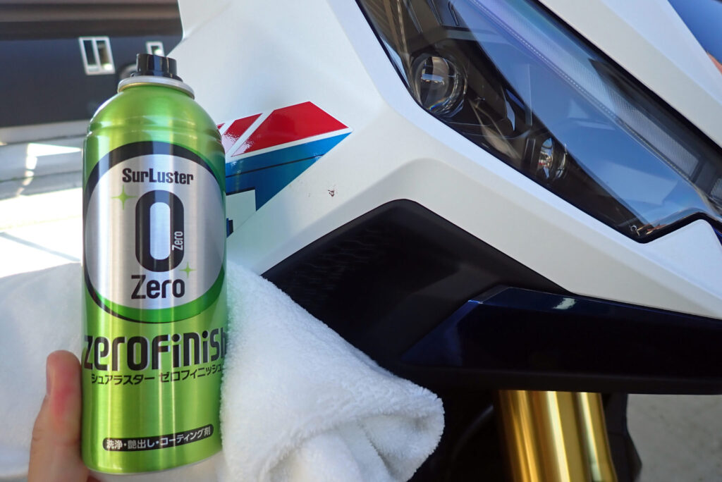 SurLuster Zero Finish spray can and microfiber cloth placed in front of a Honda X-ADV motorcycle cowl for waterless cleaning and glass coating.