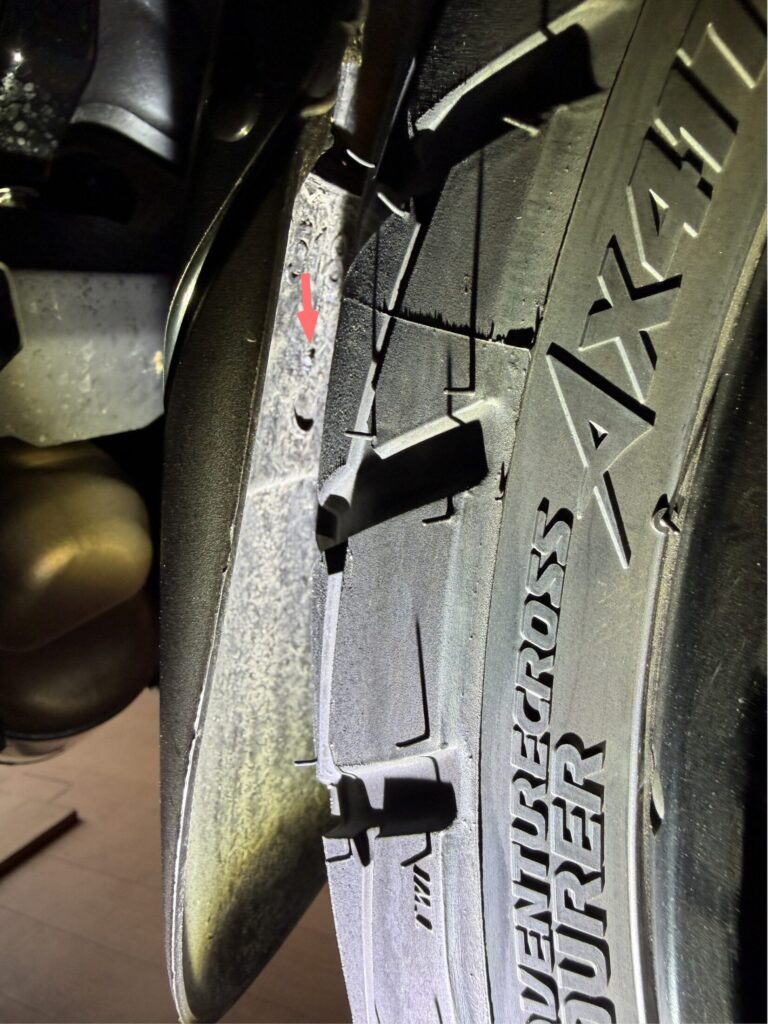 Close-up of a broken plastic safety locking pin on a motorcycle front fender, caused by interference with the tire during riding.