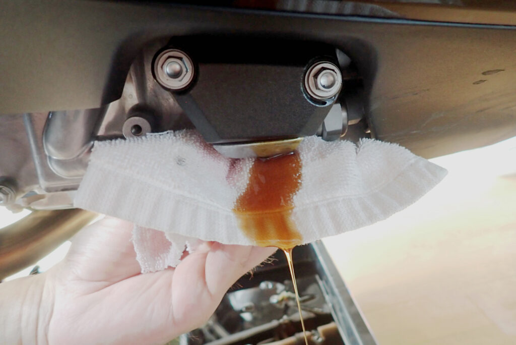 A white shop towel placed under the Honda X-ADV DCT oil filter cover to catch residual transmission oil leaking during disassembly.