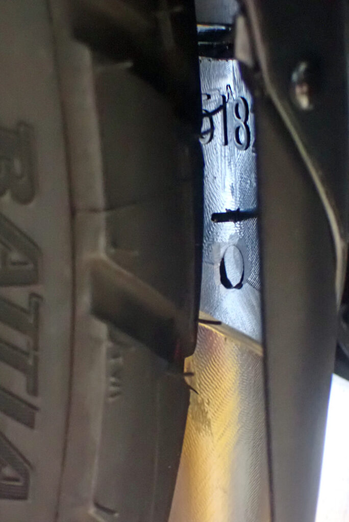Inner view of a motorcycle front fender, checking the static clearance between the newly installed safety pin tip and the tire tread.