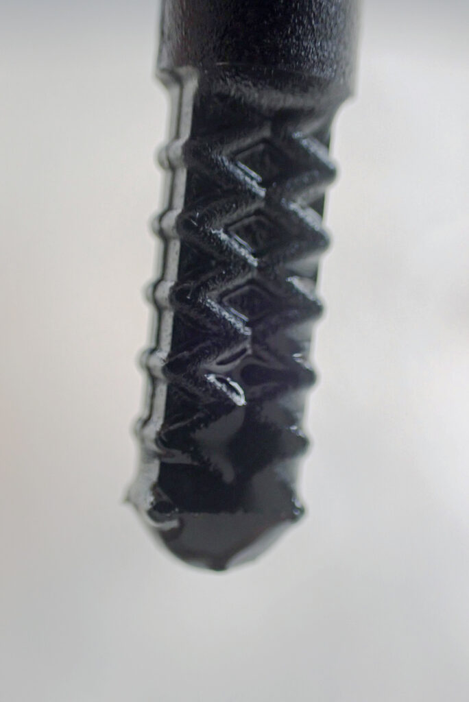 Extreme close-up of a motorcycle oil dipstick tip, showing clear fresh oil filling up the hatched cross-pattern marking correctly.