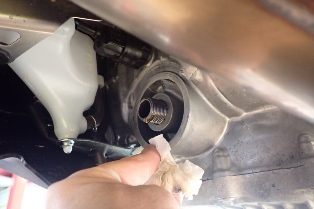 A hand using a paper towel to thoroughly clean the engine oil filter mounting base plate surface.