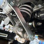 Underbody view focusing on the rear suspension linkage pivot bolts and collars ready for DIY greasing maintenance.